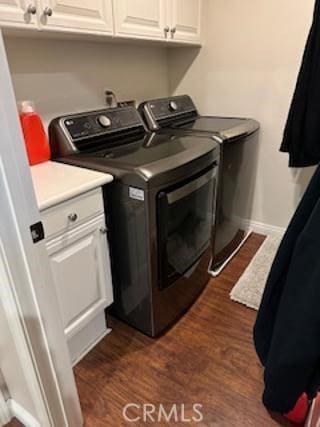 washroom featuring dark wood finished floors, washing machine and clothes dryer, cabinet space, and baseboards