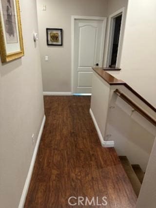 corridor featuring dark wood-type flooring, an upstairs landing, and baseboards