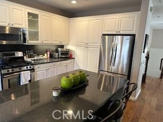 kitchen featuring stainless steel appliances, white cabinetry, dark wood-style floors, dark countertops, and glass insert cabinets