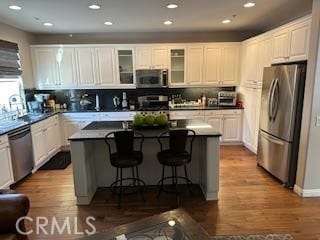 kitchen featuring dark countertops, glass insert cabinets, appliances with stainless steel finishes, a center island, and white cabinetry