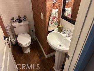 half bathroom with wood finished floors, toilet, and baseboards