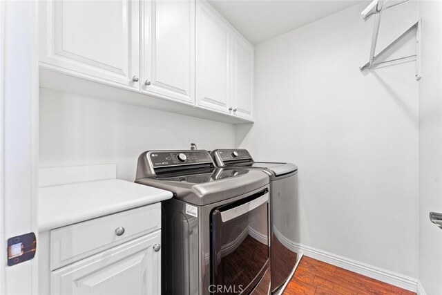 clothes washing area with washing machine and clothes dryer, baseboards, wood finished floors, and cabinet space