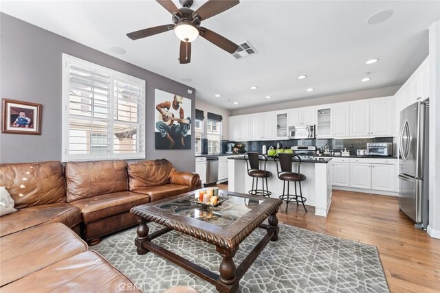 living area featuring visible vents, a ceiling fan, light wood-style flooring, and a wealth of natural light