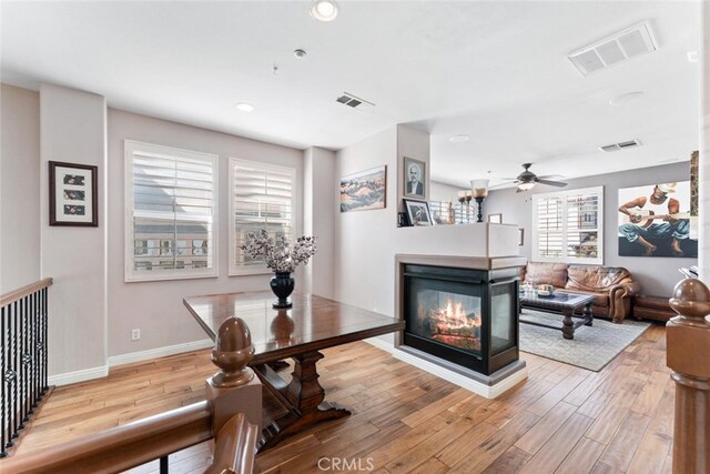 living area featuring a multi sided fireplace, baseboards, visible vents, and light wood finished floors