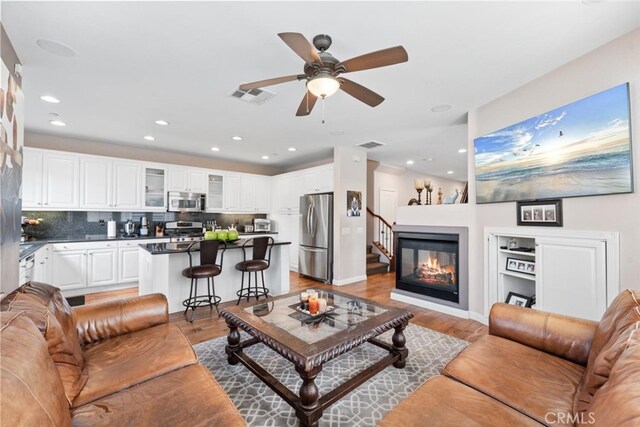 living room featuring ceiling fan, visible vents, a glass covered fireplace, recessed lighting, and light wood-style flooring