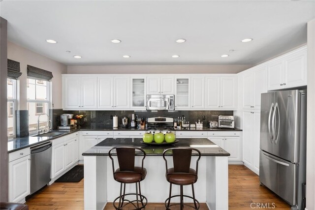 kitchen featuring stainless steel appliances, dark countertops, white cabinetry, and a sink