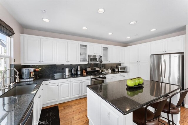 kitchen featuring backsplash, appliances with stainless steel finishes, a sink, white cabinets, and light wood finished floors