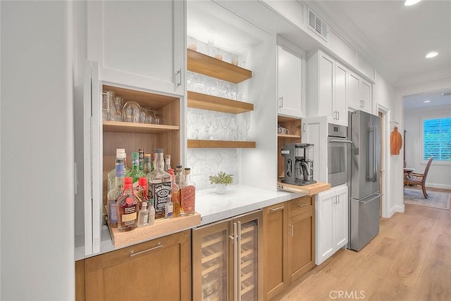 kitchen featuring white cabinetry, crown molding, light wood-type flooring, stainless steel appliances, and beverage cooler