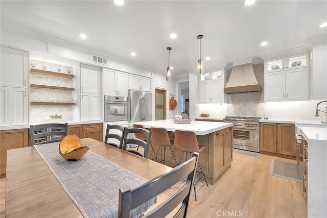 kitchen with hanging light fixtures, a center island, high end appliances, custom range hood, and white cabinets