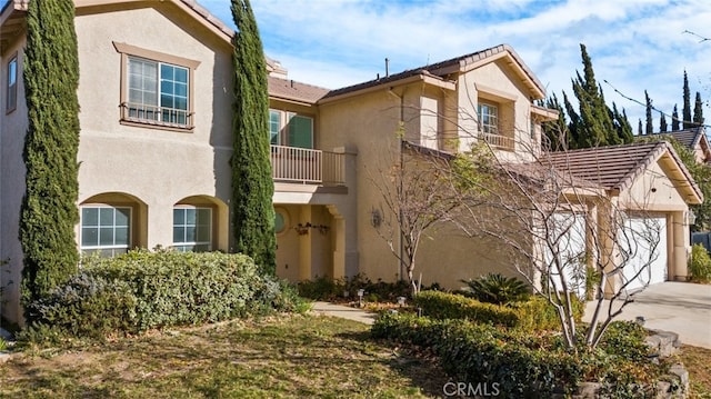 view of front of property featuring a garage, concrete driveway, a balcony, and stucco siding