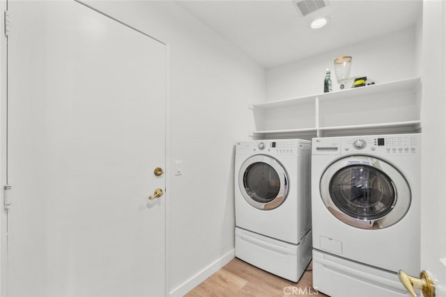 clothes washing area with laundry area, washer and clothes dryer, visible vents, and light wood-style floors