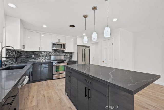 kitchen with pendant lighting, sink, appliances with stainless steel finishes, white cabinetry, and a kitchen island