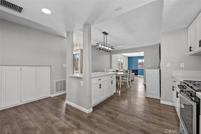 kitchen with stainless steel range with gas cooktop, pendant lighting, white cabinets, dark hardwood / wood-style flooring, and a notable chandelier