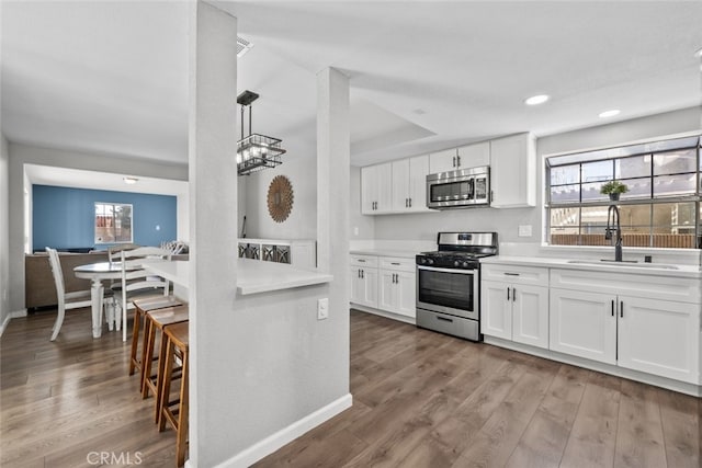 kitchen featuring stainless steel appliances, white cabinetry, sink, and pendant lighting