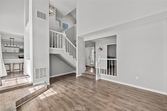 unfurnished living room with an inviting chandelier, a towering ceiling, and hardwood / wood-style flooring