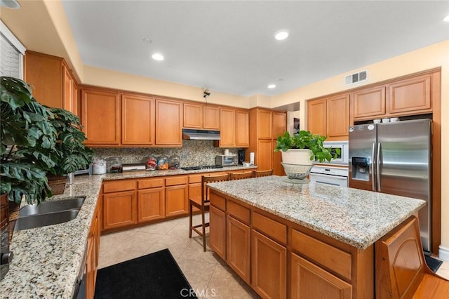 kitchen featuring sink, light stone counters, appliances with stainless steel finishes, a kitchen island, and backsplash