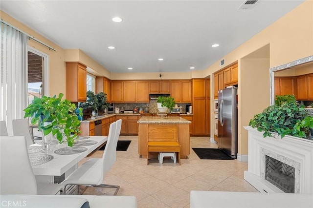 kitchen with stainless steel appliances, tasteful backsplash, light stone countertops, a kitchen island, and exhaust hood