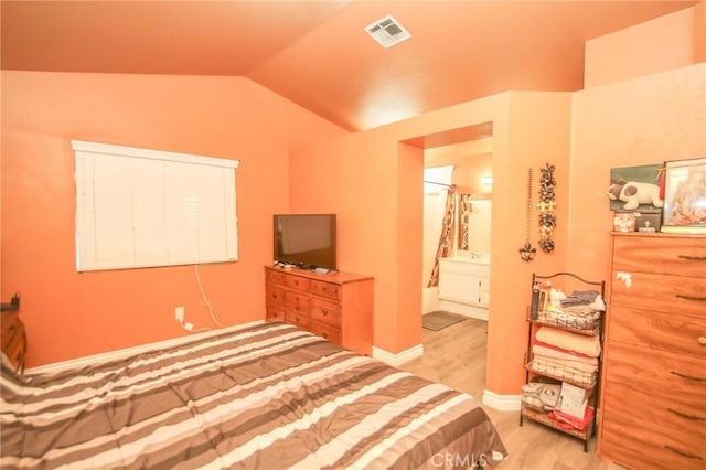 bedroom featuring vaulted ceiling, ensuite bath, and light hardwood / wood-style flooring