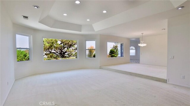 carpeted spare room with a chandelier and a raised ceiling