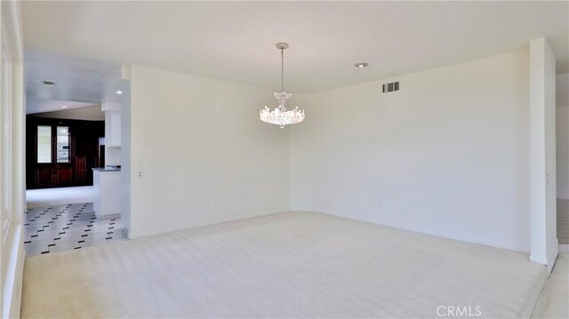 spare room featuring light carpet and a chandelier