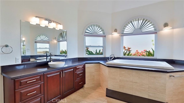 bathroom with a healthy amount of sunlight, vanity, and tiled tub