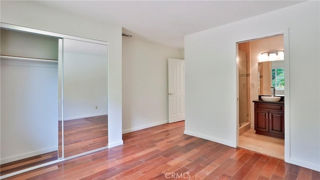 unfurnished bedroom with a sink, a closet, wood finished floors, and ensuite bathroom