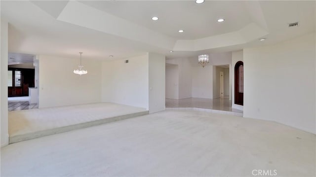 unfurnished room with visible vents, a chandelier, a tray ceiling, and light colored carpet