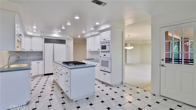 kitchen featuring a kitchen island, pendant lighting, white cabinetry, sink, and white appliances