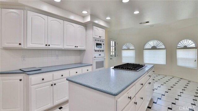 kitchen with white cabinetry, white appliances, a center island, and tasteful backsplash