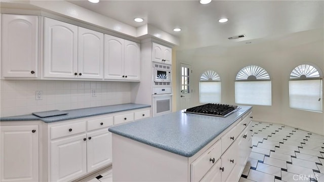 kitchen featuring white appliances, tasteful backsplash, visible vents, white cabinets, and a center island