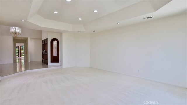 spare room featuring a chandelier, a raised ceiling, and light carpet