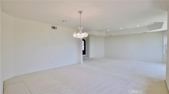 carpeted spare room featuring a notable chandelier and a raised ceiling