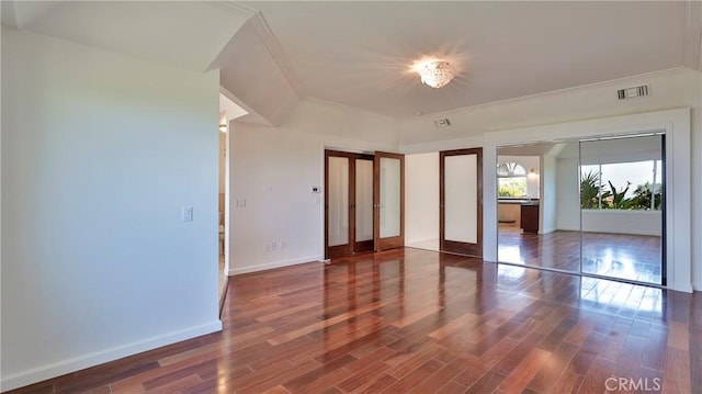 unfurnished bedroom with wood finished floors, visible vents, baseboards, multiple closets, and ornamental molding