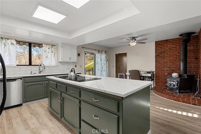 kitchen featuring dishwasher, a center island, green cabinetry, light wood-type flooring, and a wood stove