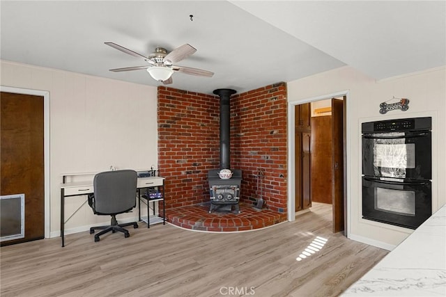 office with ceiling fan, light wood-type flooring, and a wood stove