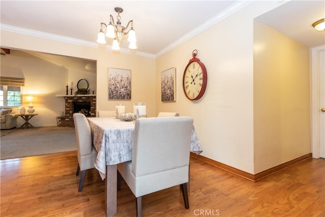 dining room with crown molding, a chandelier, a brick fireplace, and light wood-type flooring