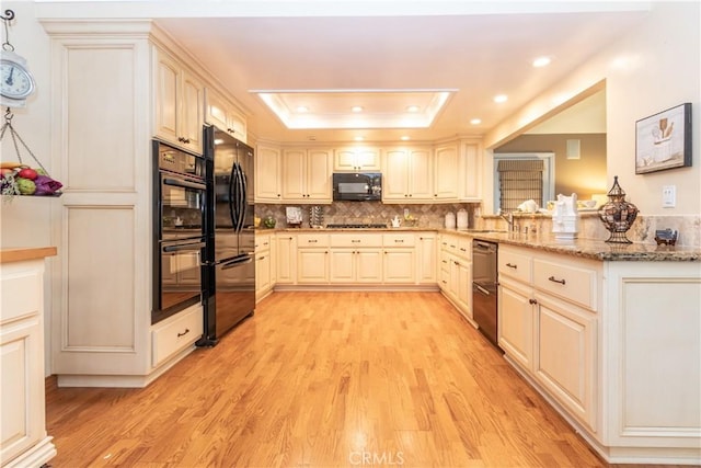 kitchen featuring a raised ceiling, light stone countertops, light hardwood / wood-style flooring, and black appliances