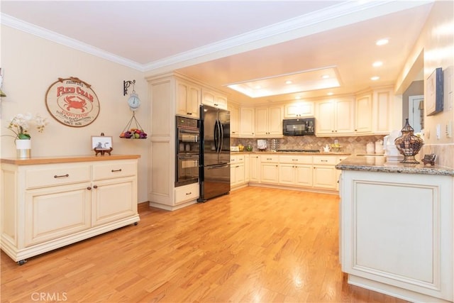 kitchen with black appliances, light wood-type flooring, ornamental molding, a raised ceiling, and backsplash