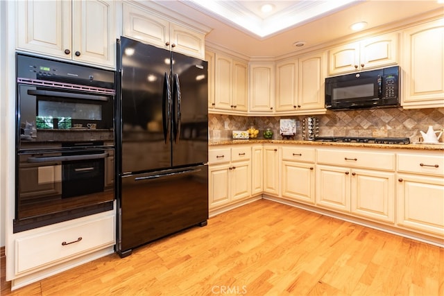 kitchen featuring backsplash, light hardwood / wood-style floors, ornamental molding, black appliances, and a raised ceiling