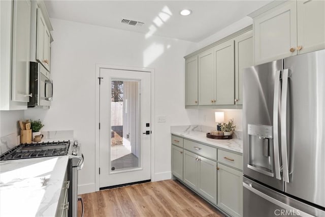 kitchen with stainless steel appliances, light stone countertops, gray cabinetry, and light wood-type flooring