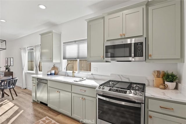 kitchen featuring sink, light hardwood / wood-style flooring, gray cabinets, stainless steel appliances, and light stone counters