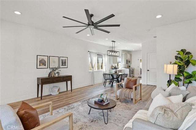 living room featuring sink, ceiling fan with notable chandelier, and light hardwood / wood-style flooring