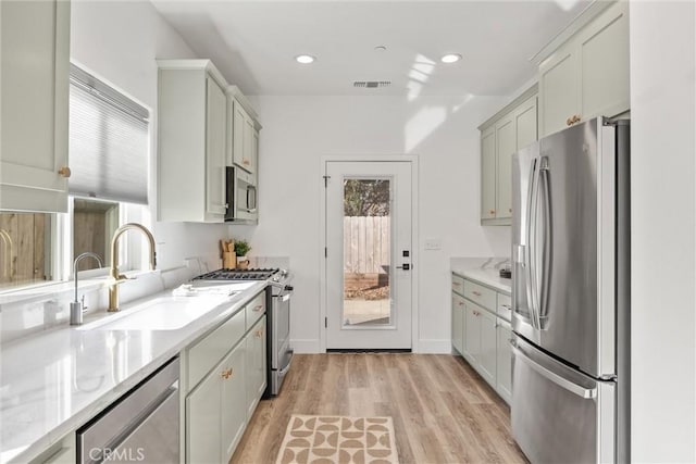 kitchen with appliances with stainless steel finishes, sink, light stone counters, and light wood-type flooring