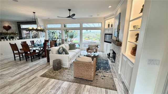 living room featuring built in shelves, ornamental molding, ceiling fan with notable chandelier, and light wood-type flooring