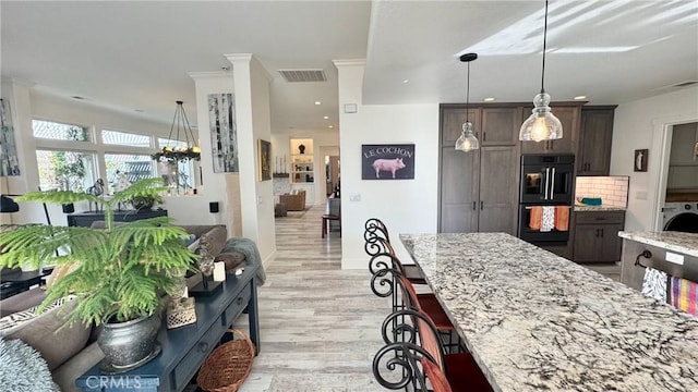 kitchen with dark brown cabinetry, light hardwood / wood-style flooring, light stone countertops, and black double oven