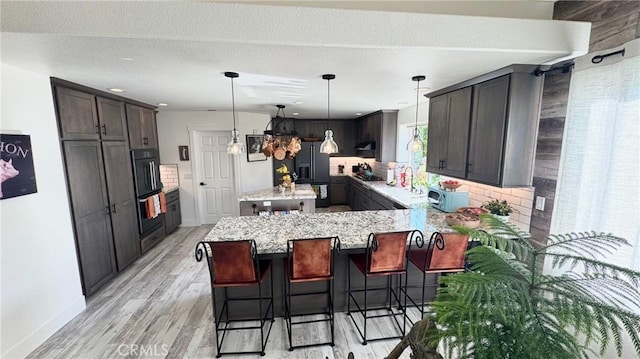 kitchen featuring a breakfast bar, pendant lighting, decorative backsplash, light stone countertops, and light hardwood / wood-style flooring