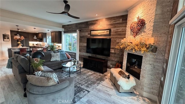 living room featuring ornamental molding, a large fireplace, ceiling fan, and light hardwood / wood-style flooring