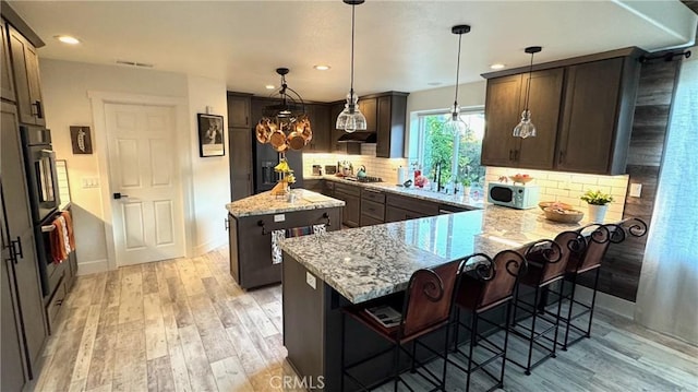 kitchen featuring a breakfast bar area, light stone counters, decorative light fixtures, a center island, and stainless steel appliances