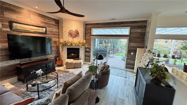 living room with a stone fireplace, crown molding, wooden walls, ceiling fan, and hardwood / wood-style floors