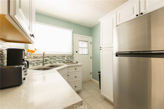 kitchen with sink, light tile patterned floors, stainless steel refrigerator, tasteful backsplash, and white cabinets